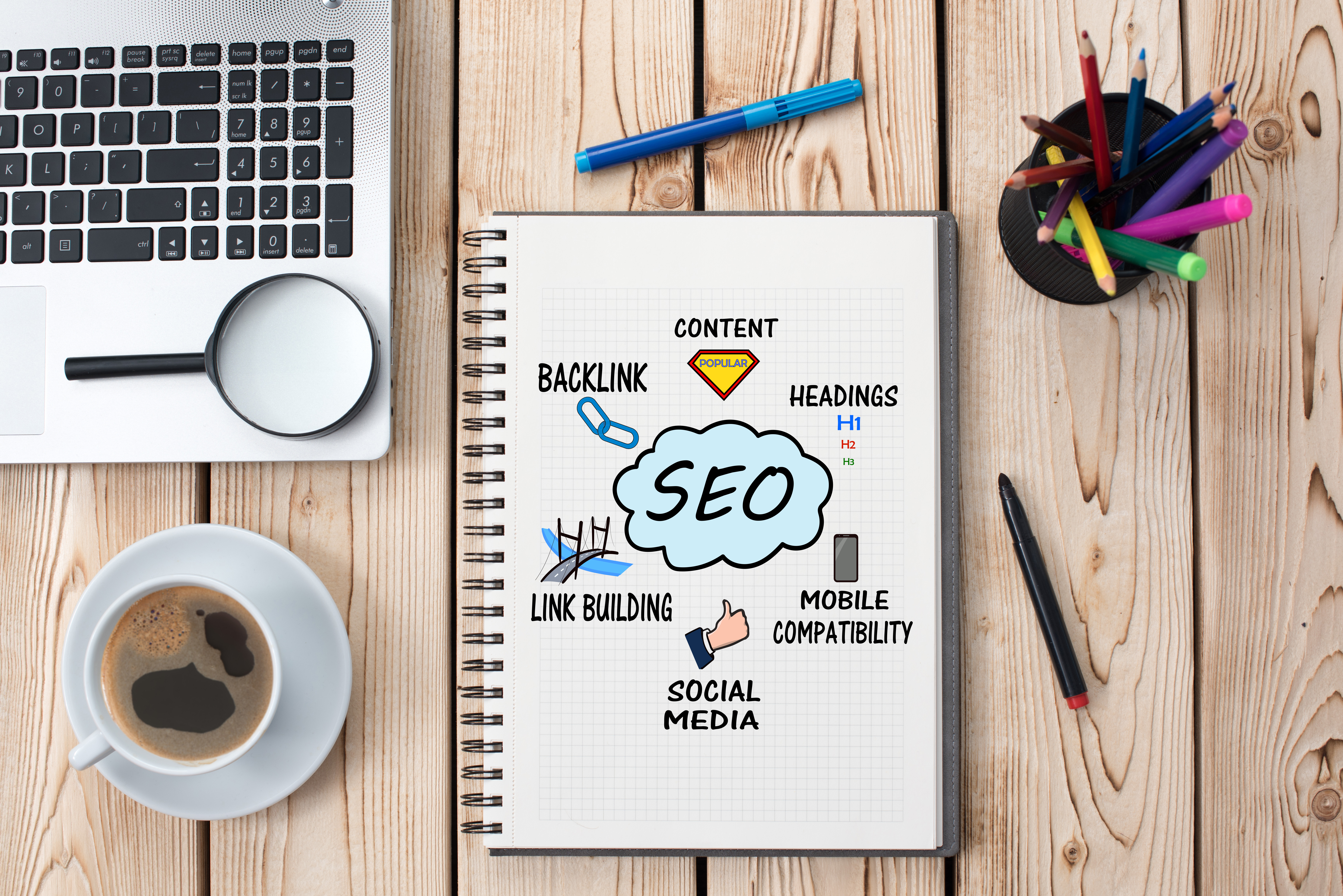 notebook placed on table, with diagram of SEO meanings, which include content, headings, mobile compatibility, social media, link building and backlinks